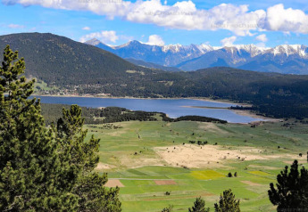 Blick auf einen See, grüne Felder und schneebedeckte Berge von einer Glamping-Unterkunft aus.