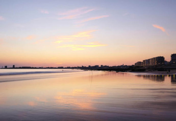 Solnedgang over stranden set fra et glamping ophold med bygninger og flotte farver i horisonten.