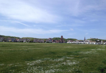 Uitzicht vanuit een strandhuis over een uitgestrekt groen veld met bloemen, huizen en een kerk.