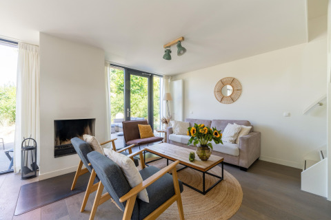 Soggiorno con arredi moderni, camino, grandi finestre e girasoli in Holiday home Waterland, Paesi Bassi.