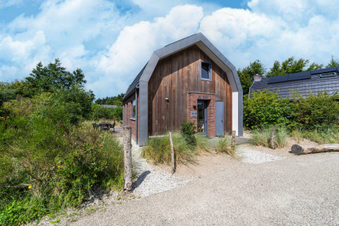Ferienhaus Waterland für sechs Personen mit modernem Holzdesign, umgeben von Natur und Kiesweg am Eingang.
