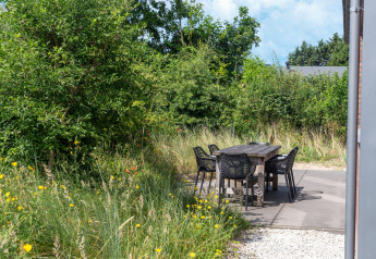 Udendørs terrasse med bord og seks stole omgivet af frodig have ved feriehus i Waterland, Holland.