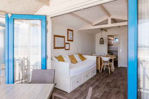 Bright beach house interior with white sofa, yellow pillows, wooden furniture and sea view through blue door.