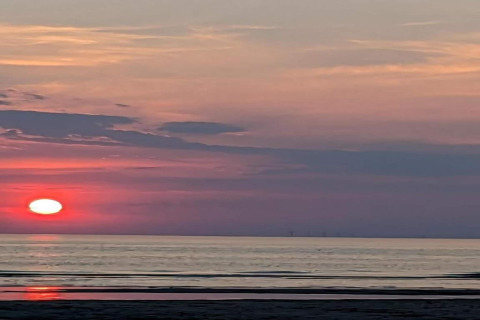 Sunset over the ocean viewed from a beach house, sky glowing with red and purple hues, beach in foreground.