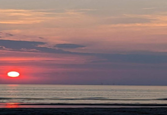 Zonsondergang boven zee gezien vanuit een strandhuis, lucht in rood en paars, strand op de voorgrond.