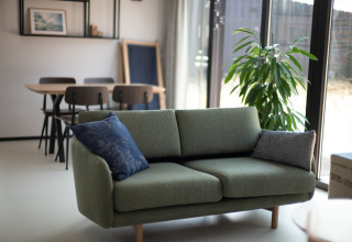 Sala luminosa con sofá verde, mesa de comedor y planta grande en Sea Lodges Zandvoort 3, Países Bajos.