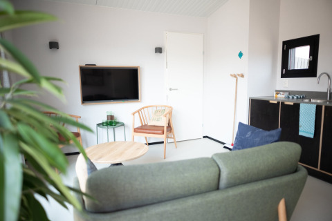 Sala de estar luminosa y moderna con sofá, TV, mesa de comedor y pequeña cocina en Sea Lodges Zandvoort 3, Países Bajos.