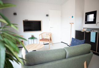 Sala de estar luminosa y moderna con sofá, TV, mesa de comedor y pequeña cocina en Sea Lodges Zandvoort 3, Países Bajos.