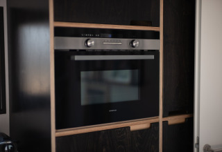 Horno empotrado moderno en una cocina de paneles oscuros, en la casa Sea Lodges «Zandvoort 3» en los Países Bajos.