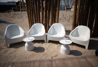 Cuatro sillas blancas modernas y dos mesas pequeñas en la arena en Sea Lodges ‘Zandvoort 3’ en los Países Bajos.