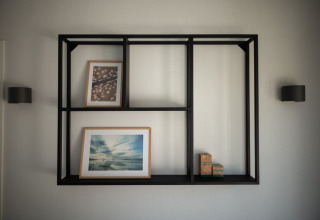 Estante moderno negro montado en la pared con cuadros y cajas, fotografiado en Sea Lodges Zandvoort 3 en Holanda.