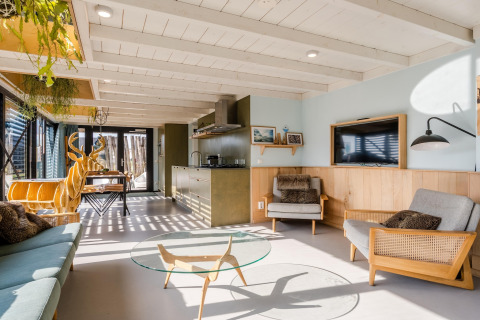 Casa de playa luminosa con muebles modernos de madera, ventanales grandes y ambiente acogedor.