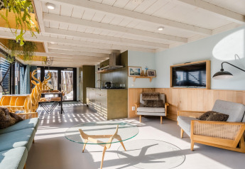 Helles Strandhaus mit modernen Holzmöbeln, offenem Wohnbereich, Glaswand und sonniger Atmosphäre.