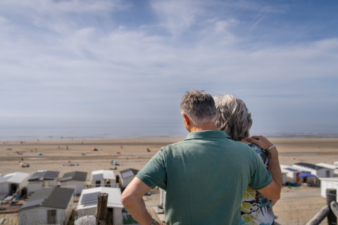 Pareja de personas mayores abrazadas observa la playa y el mar desde su casa en la playa en un día soleado.