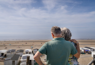 Pareja de personas mayores abrazadas observa la playa y el mar desde su casa en la playa en un día soleado.