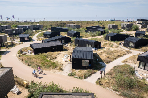 Vista aérea de casas de playa negras modernas cerca de la costa, ciclistas en senderos y paisaje de dunas.