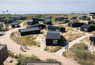 Vista aérea de casas de playa negras modernas cerca de la costa, ciclistas en senderos y paisaje de dunas.