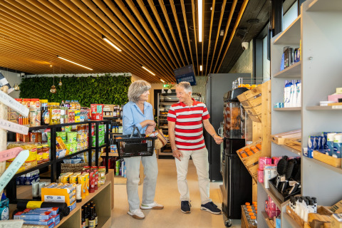 Dos personas mayores hacen la compra en una tienda moderna con techo de madera y estantes llenos.