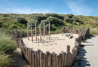 Zona de ejercicios al aire libre en una casa de playa con postes de madera, barras y suelo de arena.