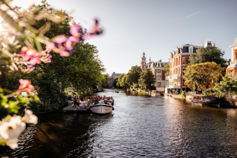 Vista de un canal en Ámsterdam con barcos, árboles y edificios históricos en un día soleado en los Países Bajos.