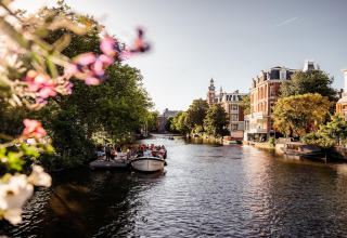 Vista de un canal en Ámsterdam con barcos, árboles y edificios históricos en un día soleado en los Países Bajos.