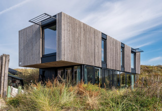 Casa de playa moderna con fachada de madera y grandes ventanas en las dunas de Zandvoort, Países Bajos.
