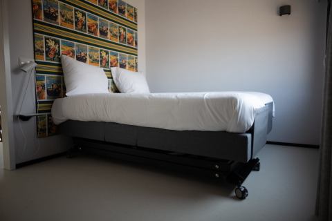 Cama moderna con ruedas y sábanas blancas junto a papel tapiz colorido en Sea Lodges Zandvoort 1, Países Bajos.