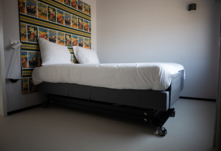 Cama moderna con ruedas y sábanas blancas junto a papel tapiz colorido en Sea Lodges Zandvoort 1, Países Bajos.