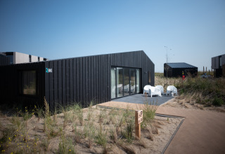 Casa moderna Sea Lodges Zandvoort 1 en los Países Bajos, rodeada de dunas y sillas blancas afuera.