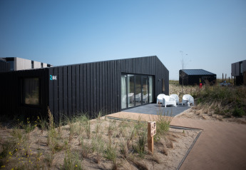 Moderne schwarze Strandlodge Sea Lodges Zandvoort 1 in den Niederlanden, umgeben von DĂĽnen und Sand.