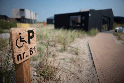 Señal de aparcamiento accesible en Sea Lodges Zandvoort 1 con camino y césped de dunas en los Países Bajos.