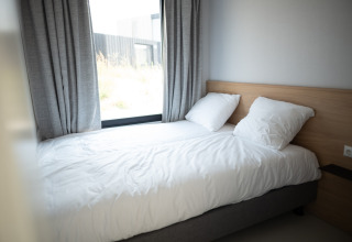 Lichte slaapkamer met een enkel bed, witte lakens, twee kussens en een groot raam bij Sea Lodges Zandvoort 1.