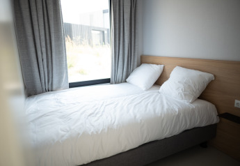 Helles Schlafzimmer mit Einzelbett, weiĂźen BettbezĂĽgen, zwei Kissen und groĂźem Fenster in Sea Lodges Zandvoort 1.