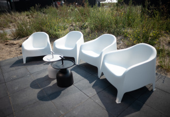 Vier weiĂźe Outdoor-StĂĽhle und zwei Tische auf der Terrasse bei Sea Lodges Zandvoort 1 in den Niederlanden.