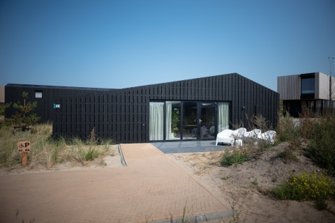 Modern strandhuis Sea Lodges Zandvoort 1 met donkere gevel en terras onder een heldere blauwe lucht.