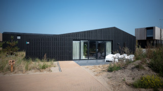 Casa de playa moderna Sea Lodges Zandvoort 1 con fachada oscura y terraza bajo un cielo azul despejado.