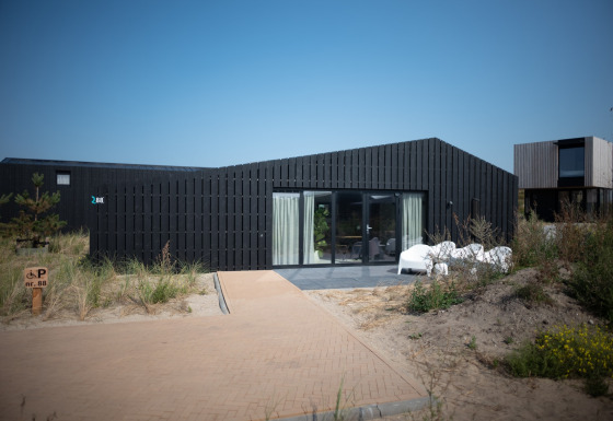 Modern strandhuis Sea Lodges Zandvoort 1 met donkere gevel en terras onder een heldere blauwe lucht.