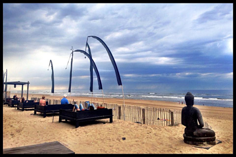 Glampingverblijf aan zee met zithoeken, vlaggen en een Boeddhabeeld onder een bewolkte hemel.