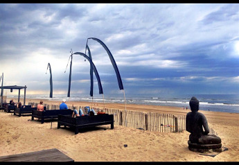 Glamping-Unterkunft am Strand mit Sitzbereichen, Flaggen und Buddha-Statue bei bewölktem Himmel.