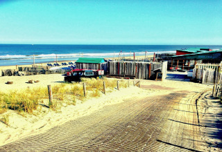 Vista de la casa de playa Sea Lodges «Zandvoort 1» en Países Bajos con arena, mar y tumbonas azules.