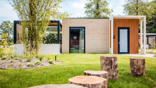 Lodge moderno con sedute in tronchi di legno in un giardino verde, circondato da alberi e luce naturale.