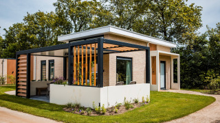 Modern lodge with spacious terrace, pergola, and garden, surrounded by lush greenery and trees.
