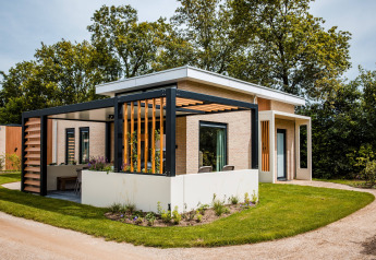 Moderne lodge met ruime pergola, terras en tuin, gelegen tussen grasvelden en bomen.