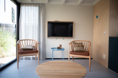Sala luminosa en Sea Lodges Zandvoort 4 con dos sillas de madera, cojines, mesa pequeña y televisor.
