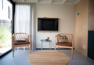 Sala luminosa en Sea Lodges Zandvoort 4 con dos sillas de madera, cojines, mesa pequeña y televisor.