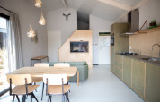 Modernes Wohnzimmer und Küche in den Sea Lodges Zandvoort 3 mit Esstisch und grünem Sofa.