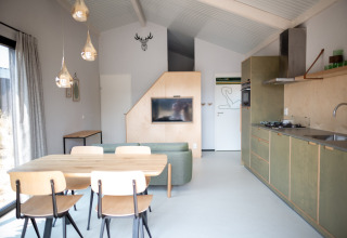 Acogedora sala y cocina en Sea Lodges Zandvoort 3, con mesa de comedor y sofá verde con luz natural.