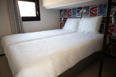 Dormitorio en Sea Lodges Zandvoort 3 en los Países Bajos con dos camas, sábanas blancas y carteles de carreras.