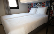 Schlafzimmer im Sea Lodges Zandvoort 3 in den Niederlanden mit zwei Betten, weißen Laken und Rennplakaten.