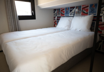 Schlafzimmer im Sea Lodges Zandvoort 3 in den Niederlanden mit zwei Betten, weißen Laken und Rennplakaten.